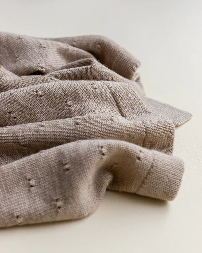Close-up image of a Handmade Merino Wool Bibi Blanket - Sand with small, raised pimple-like details, elegantly crumpled on a light surface.