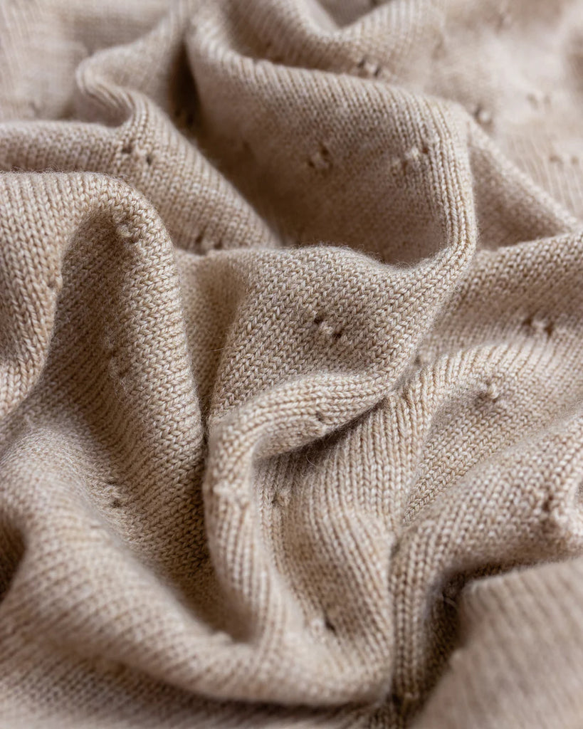 Close-up of a textured sand Handmade Merino Wool Bibi Blanket showing detailed stitch patterns and soft folds.