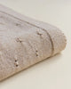 Close-up of a sand colored textured Bibi blanket folded neatly, showing detailed stitch patterns and small embroidered elements on the fabric.