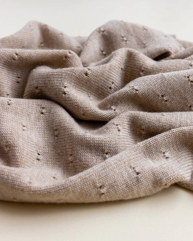 A close-up image of a Handmade Merino Wool Bibi Blanket - Sand with small, raised bumps scattered throughout, gracefully folded and draped on a light background.