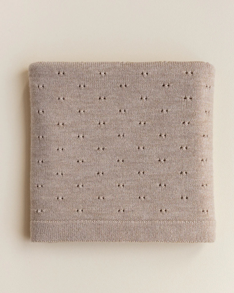 A neatly folded Handmade Merino Wool Bibi Blanket - Sand with a pattern of small, evenly spaced holes, displayed on a light-colored background.