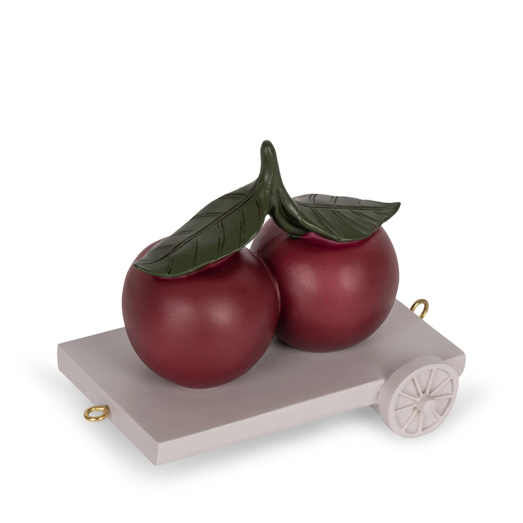 The Magical Forest Birthday Train With Beeswax Candles showcases two large red cherries with green leaves on a small white wheeled platform, set against a plain white background.