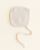 A Cream handmade Merino Wool newborn bonnet with a pair of string ties, placed on a soft beige background.