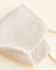 A soft, white knitted Handmade Merino Wool Newborn Bonnet - Cream made from eczema-sensitive skin-friendly material folded neatly on a light beige background.