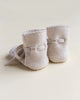 A pair of Handmade Merino Wool Booties in a soft cream color, displayed upright with the laces gently tied, set against a light beige background.