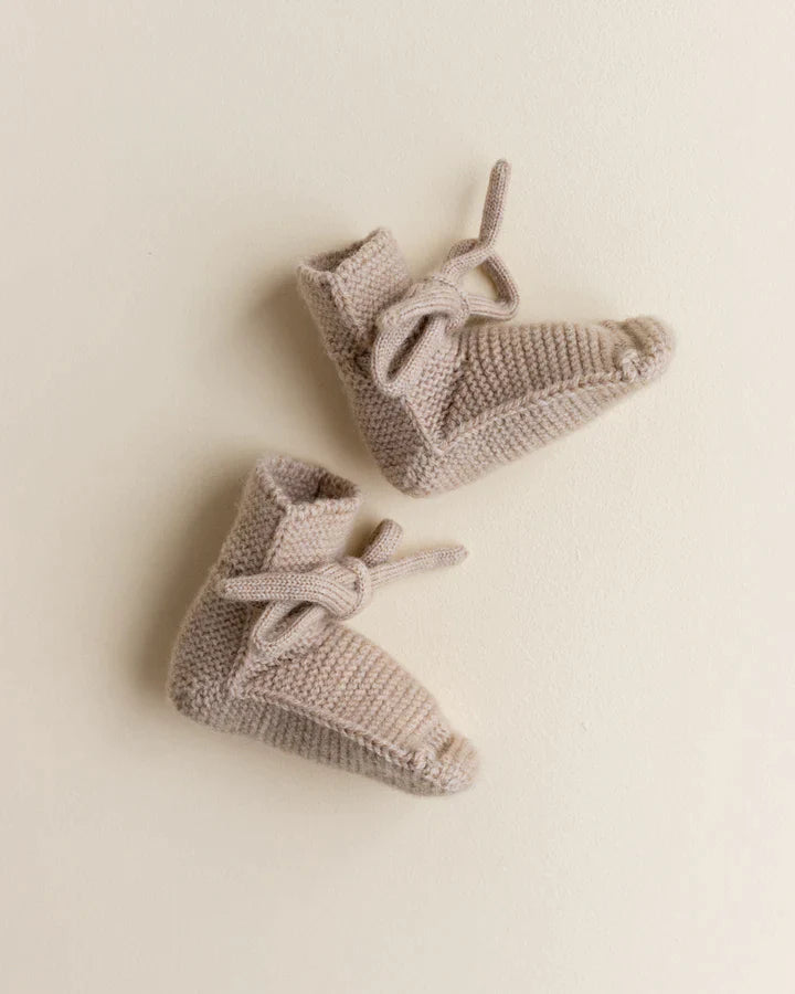 A pair of Handmade Merino Wool Booties - Sand in a soft beige color, delicately placed on a plain light background. The booties, made from eczema-friendly merino wool, feature laces.