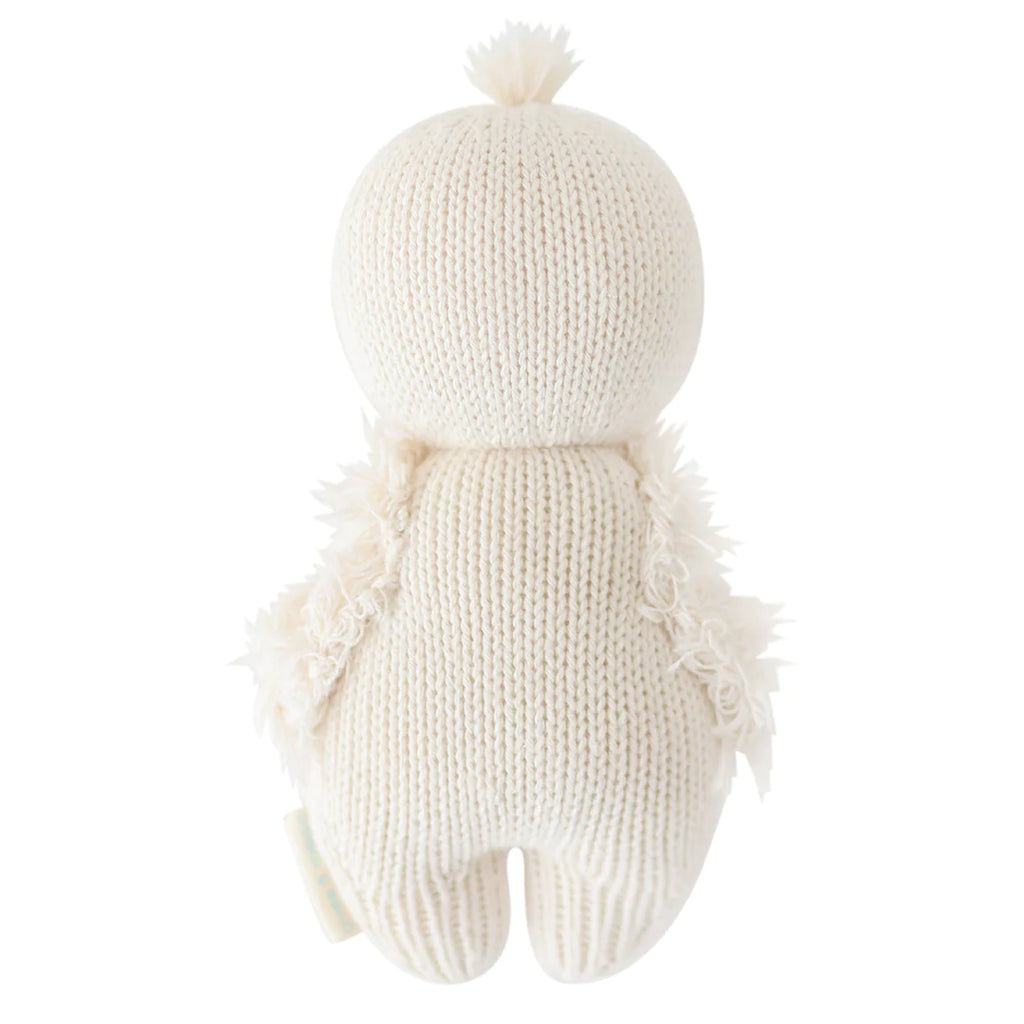 A soft, hand-knit cream-colored Cuddle + Kind Baby Gosling plush toy with a cute pompom on top of its head and fluffy textures on its tentacles, isolated on a white background.