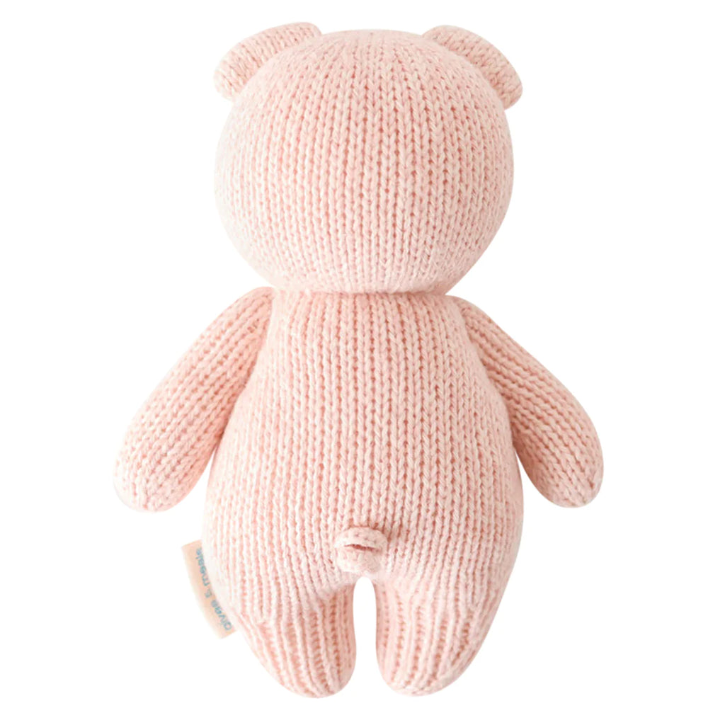 A soft, pink hand-knit Cuddle + Kind Baby Piglet with visible stitches, upright ears, and no facial features on a white background.