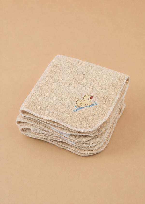 A set of Konges Sloejd Organic Cotton Baby Cloths (6 Pack) is neatly folded, with the top beige cloth adorned with a charming embroidered yellow duck holding a red heart on a blue branch. Arranged on a plain, light brown surface, these nursery cloths are perfect for any gentle care routine.
