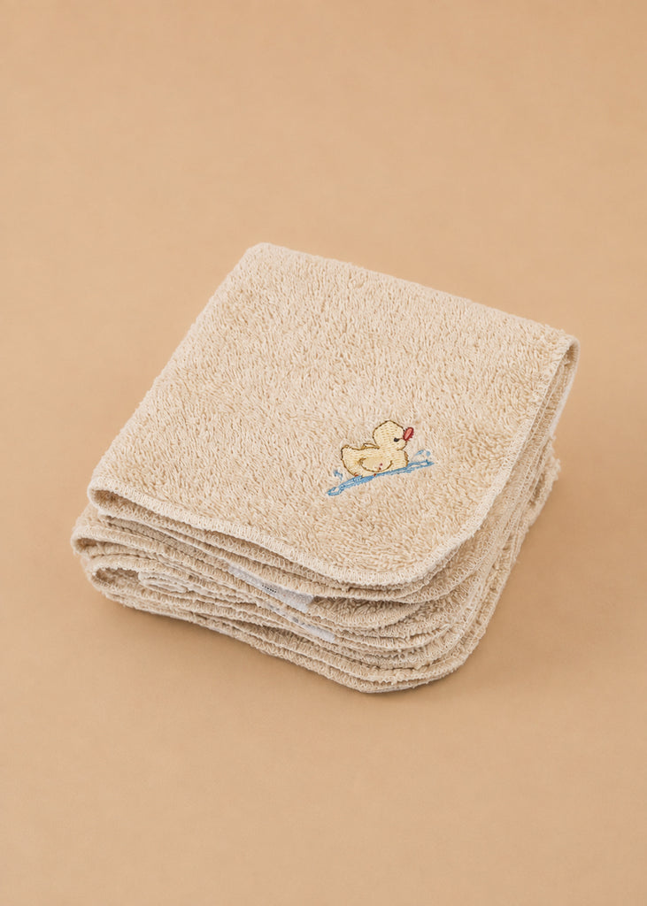 A set of Konges Sloejd Organic Cotton Baby Cloths (6 Pack) is neatly folded, with the top beige cloth adorned with a charming embroidered yellow duck holding a red heart on a blue branch. Arranged on a plain, light brown surface, these nursery cloths are perfect for any gentle care routine.