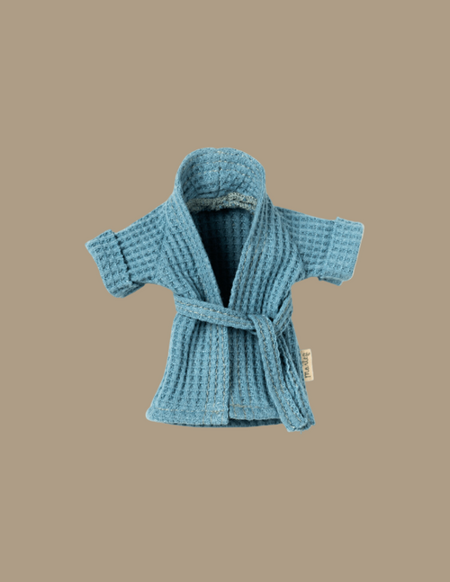 A small blue waffle-knit Maileg Extra Clothing: Bathrobe - Dusty Blue with a belt tied around the waist. The robe has short sleeves and an open front, revealing its soft, textured fabric inside. The background is a plain light beige color.