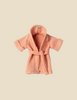 A textured, peach-colored cotton polyester Maileg Extra Clothing: Bathrobe - Coral with short sleeves and a waist tie is displayed against a beige background. The soft bathrobe appears absorbent, suitable for casual lounging or post-bathing comfort.