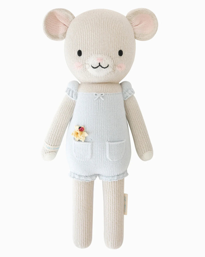 Cuddle + Kind Beatrice The Mouse - Periwinkle: a beige knitted mouse handmade with hypoallergenic polyfill, wearing a periwinkle romper with a yellow flower, rosy cheeks, and a gentle smile against a white background.