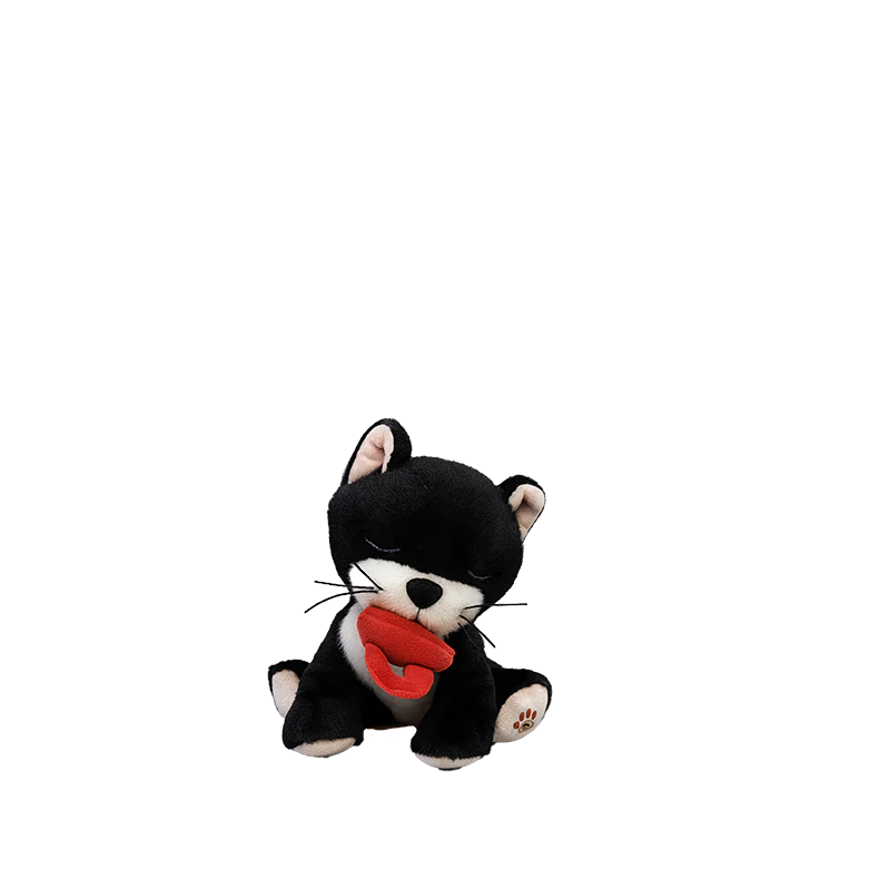 The Olli Ella Binky Kitten Kit - Black & White is a small plush with closed eyes, sitting upright and holding a red heart in its mouth, shown against a plain white background.