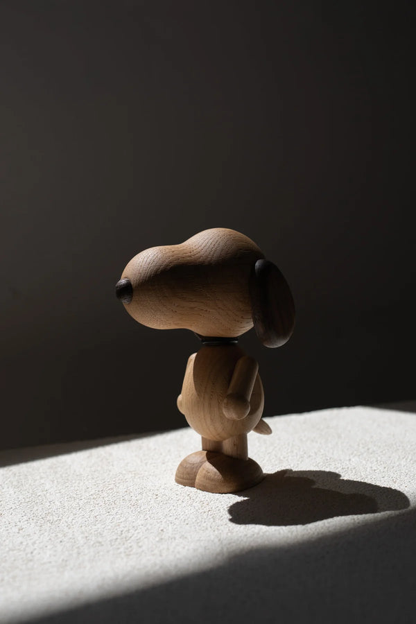 A Boyhood Snoopy, Large figurine, creatively sculpted with smooth curves and minimal details, stands highlighted by a sharp beam of light casting a dramatic shadow on a muted background.