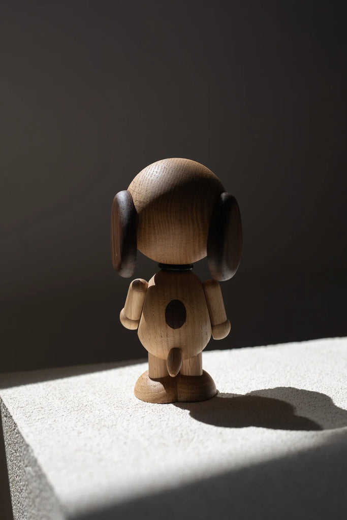 A Boyhood Snoopy, Large figurine with a round head and simplistic body features stands on a ledge, highlighted by a dramatic shaft of light against a dark background.