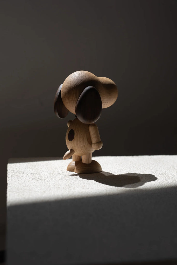 A Boyhood Snoopy, Large figurine, with exaggerated features, stands on a light surface under dramatic lighting that creates a sharp shadow.