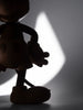Silhouette of a Mickey Mouse, Oak figurine stands against a bright, soft-focus, light gray background. Partially visible, it echoes Mickey's adventurous spirit with its large round shoes and gloved hands.