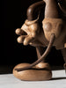 The "Mickey Mouse, Oak" sculpture highlights Mickey's iconic status with exaggerated gloves, round shoes, and a long tail. It captures his adventurous spirit as he stands on a light surface against a dark background.