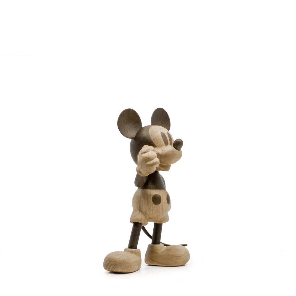 The oak sculpture of the global icon Mickey Mouse stands against a white background with green distortion. It features large round ears, a short tail, and buttoned shorts, capturing his adventurous spirit.