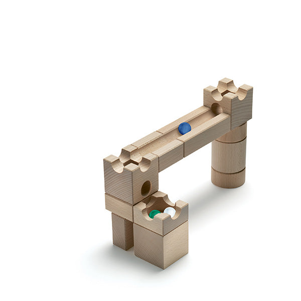 A wooden toy arch structure with interlocking pieces, featuring a rolling blue marble in the Cuboro Magnet Marble Run Extra Set system and a green ball below in a hole.