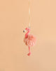 The Bukowski - Phoebe Flamingo Bag Charm, a fluffy pink plush flamingo keychain with a yellow ribbon, hangs against a plain light peach background—making it the perfect adorable accessory for your bag or keys.