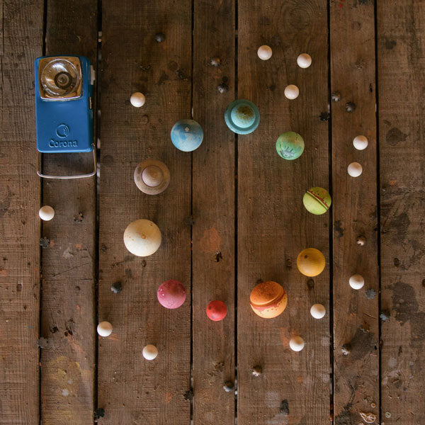 A vintage corona camera lay on a wooden surface surrounded by colorful Grapat Dear Universe planets arranged in a random pattern.