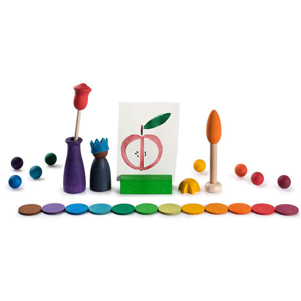 A playful, colorful setup featuring miniature sculpted items from Grapat Your Day: two trees, a bush, and an easel with a painting of an apple, surrounded by multicol