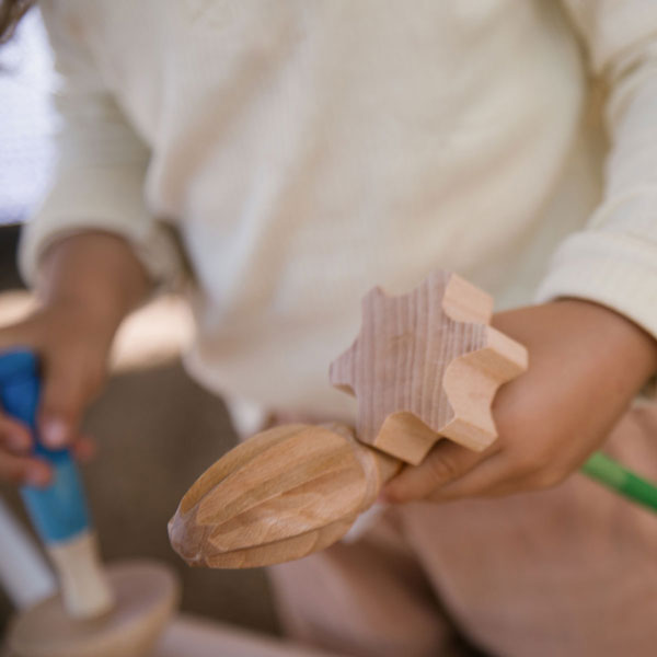 Adult hands a Grapat Tools wooden toy airplane to a child in a playful and educational setting. Close-up view emphasizing the exchange and focus on sustainable wooden toys.