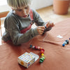 A child threads colorful wooden beads onto a string at a table covered with a rust-colored cloth, while an open box with patterns—part of the Grapat Christmas Advent Calendar 2026 (Final Sale, ships in approximately two weeks)—sits nearby, sparking creative family holiday activities.