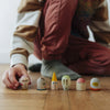 A child in striped clothes kneels on a wooden floor, arranging six small, painted wooden figures with unique faces and shapes in a row—a heartwarming scene reminiscent of family holiday traditions, such as discovering the surprises inside the Grapat Christmas Advent Calendar 2026 - Final Sale (ships in approximately two weeks).