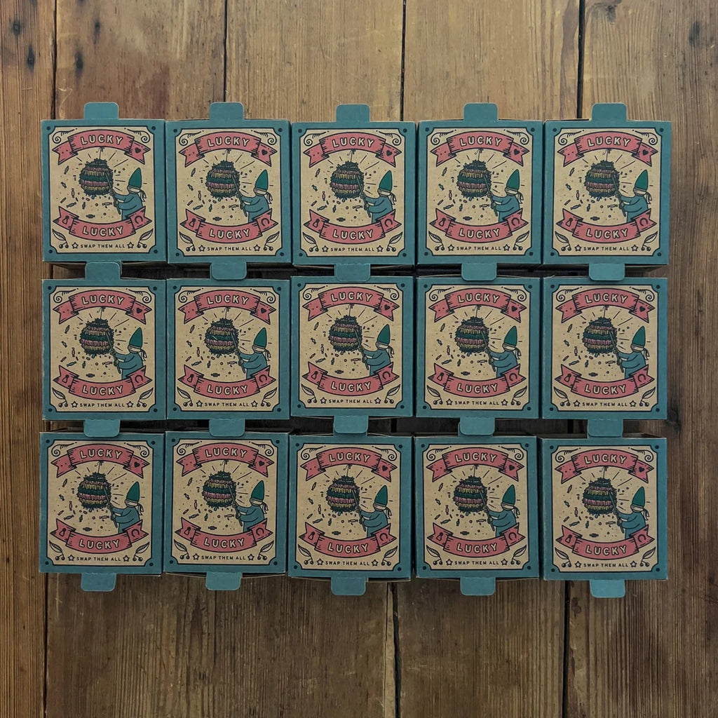 Twelve boxes of the Grapat Lucky Lucky Surprise Set 5th Edition—each featuring a charming bee illustration—are arranged in three rows on a wooden surface, inviting discovery of collectible toys and delightful mystery treasures inside.