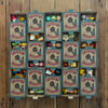 Sixteen small boxes from the Grapat Lucky Lucky Surprise Set 5th Edition are arranged in a grid on a wooden floor. Each mystery box is partly open, revealing an assortment of colorful collectible toys and objects inside each compartment.