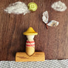 A whimsical scene unfolds with the Grapat Lucky Lucky Surprise Set 5th Edition: a wooden figure in a yellow hat sits upon a log, while overhead, cotton clouds, a green button sun, and a butterfly crafted from paper and twig drift by—capturing the collectible toy magic the set is renowned for. Beneath it all, a checkered cloth mimics flowing water, transforming this display into an enchanting miniature world as delightful as unboxing your own surprise treasure.