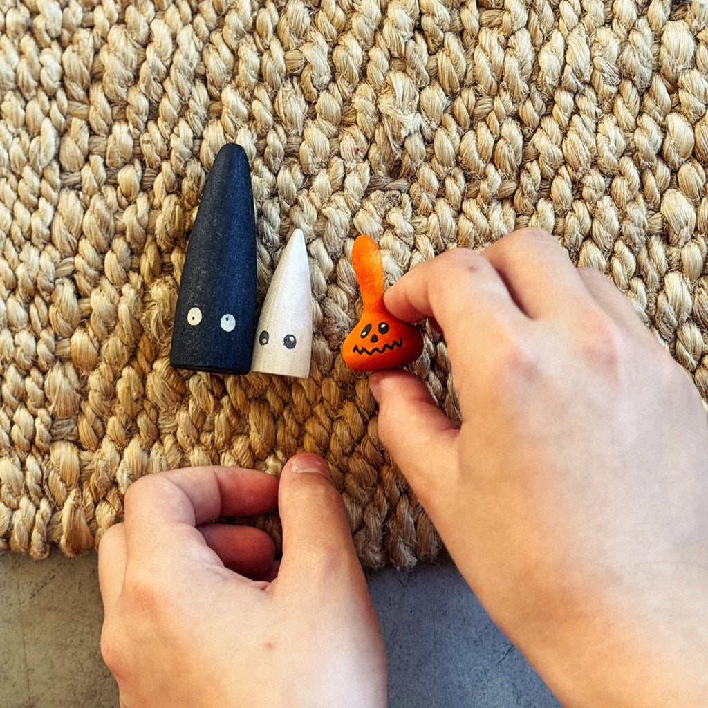 Two hands hold small, painted collectible toys with eyes—one black, one white, and one orange with a jack-o’-lantern face—from the Grapat Lucky Lucky Surprise Set 5th Edition, displayed on a woven mat as if just discovered from the surprise box set.