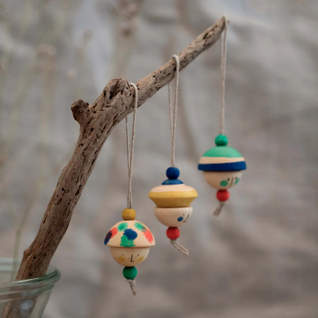 Three small, hand-painted figures from the Grapat Ornament Set - No 8 - Kind Folks hang by strings, each with colorful patterns and beads, perfect for festive decor on a branch or tree.