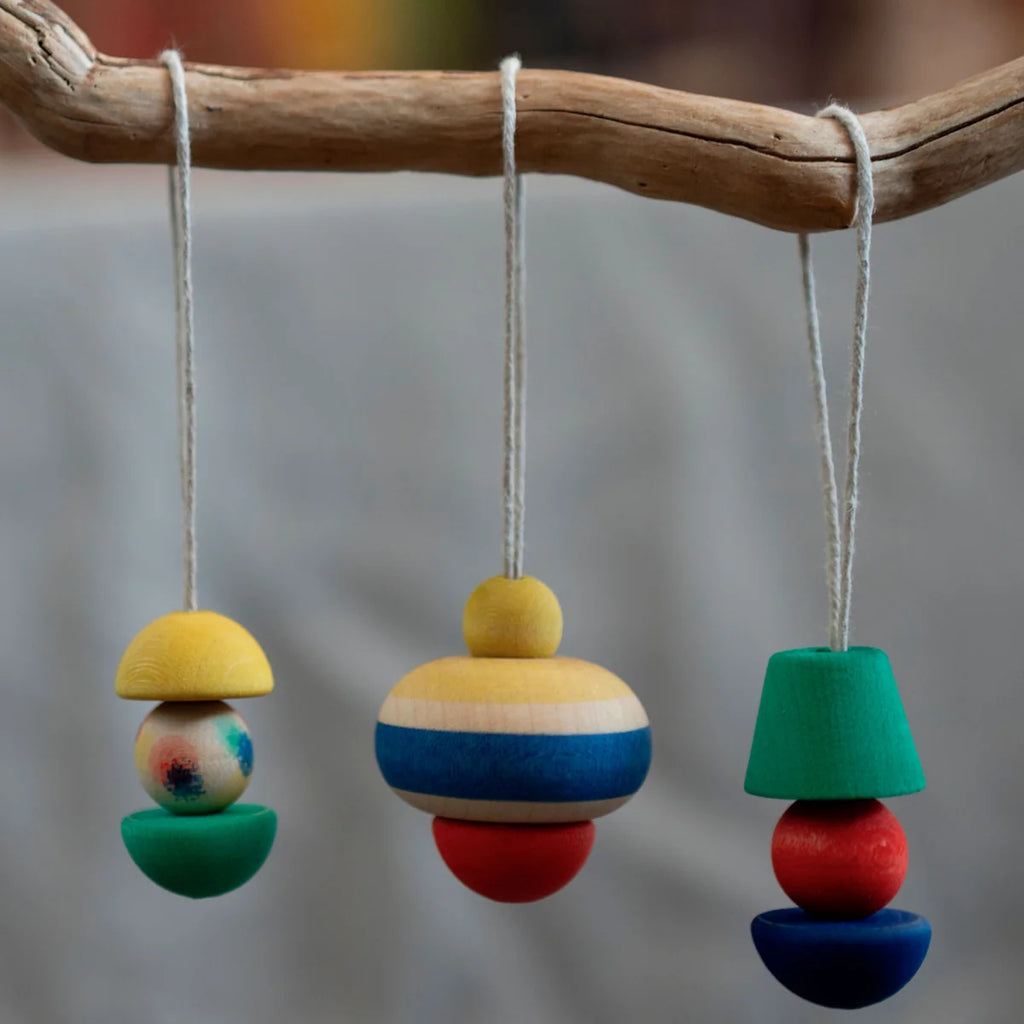 Three vibrant geometric ornaments from the Grapat Ornament Set - No 9 - Pure Shine hang on white strings. Each wooden piece is stacked in unique shapes and bright colors: yellow, blue, red, and green.