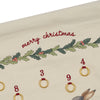 Close-up of a cream-colored Christmas Calendar (Final Sale) with "Merry Christmas" embroidered in red, green holly leaves, and red berries, with organic cotton brass rings numbered 3, 4