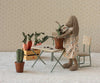 The Maileg Bunny, Size 2 - Brown - Dress stands by a small table, repotting a fabric plant. Soft natural fabrics form nearby plants and veggies, with tiny furniture and a crate in the background.