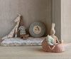A cozy children's play area features plush toys—a giraffe, two striped rabbits, a bunny bed, a mountain cushion—and the Maileg Carry Cot, Large - Rose as a pink basket holding stuffed animals, all atop a wooden floor.