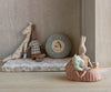 The Maileg Rabbit, Size 3 - Brown, dressed in a shirt and shorts, is arranged with other stuffed animal toys on a floral cushion beside a round mountain pillow. The rabbit sits in a pink basket with small plush toys.