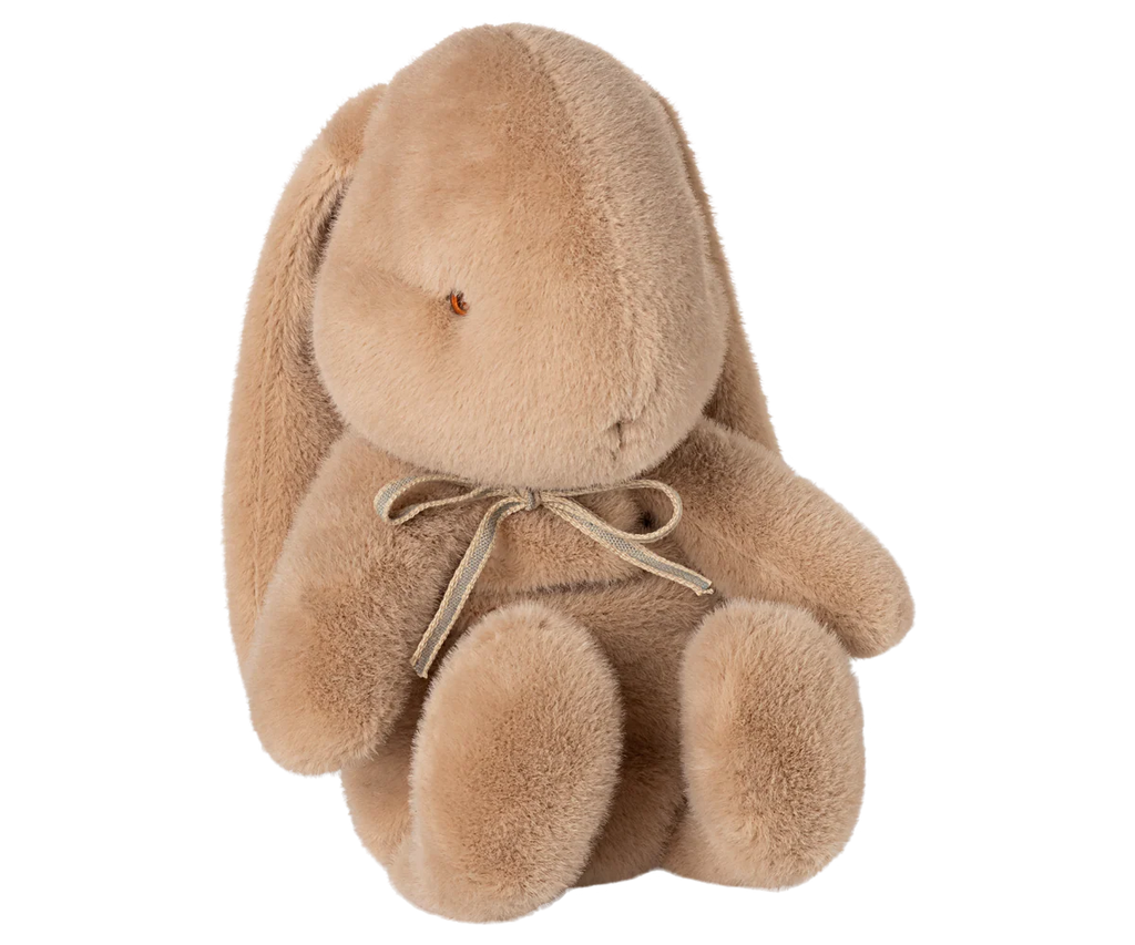 The Maileg Plush Bunny, Medium - Cream Peach, is a soft light brown toy with long floppy ears, round limbs, and a small bow around its neck, shown sitting upright against a plain white background.