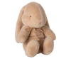 The Maileg Plush Bunny, Small - Latte is a soft light brown stuffed animal with floppy ears, simple stitched eyes and nose, and a small bow around its neck, shown sitting upright against a plain white background.