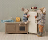 Two toy mice enjoy ice cream by the Maileg Fridge, Mouse - Off White in their kitchen, surrounded by dollhouse accessories. One sits on the counter while the other stands near a cheese wedge and fish toy, creating a cozy farmhouse scene.