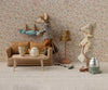 Two mice tidy their Mouse hole Farmhouse: one hangs laundry above the Maileg Couch, Mouse Size - Mable, while the other vacuums near a tea set in a vintage room with floral wallpaper and a lamp.