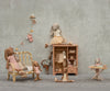 A group of stuffed bunnies in pastel clothes play in a cozy room featuring the Maileg Wardrobe, Large - Dark Powder, alongside a sofa, ironing board, and bunting against a neutral textured wall.