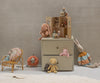 A children’s room with a small Maileg SuitCasa (mice and furniture sold separately, ships in one week), topped by a dollhouse and plush toys, plus more stuffed animals, a toy rattan chair, and a bedding-included portable mouse house on a white rug.