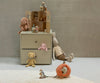 A small dresser with two drawers holds a dollhouse and stuffed animals, including the Maileg Plush Bunny, Medium - Vintage Rose, plus a bear and mouse. More plush toys and a pumpkin-shaped carriage sit on the floor by a white rug against a gray wall.