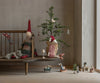A Maileg Christmas Mouse, Maxi - Girl sits on a wooden bench by a small decorated tree, surrounded by miniature furniture and festive holiday decorations. Ships in one week.