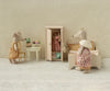 Three toy mice, dressed in clothes, are in a miniature room with a bed, a Maileg Mini Side Table topped with pastries, a chair, and an open wardrobe displaying hanging outfits. The scene features a neutral, vintage style.